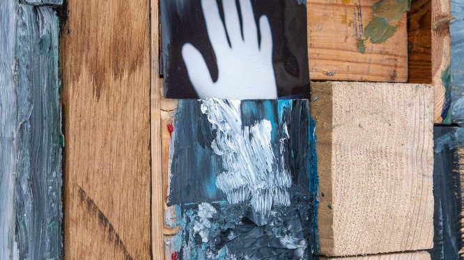Obrys dłoni i czarno-biały abstrakcyjny obraz w ramie z drewnianych elementów.