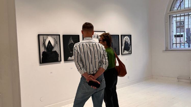 Odwiedzający wystawę mężczyzna i kobieta oglądają zdjęcia wiszące na ścianach.