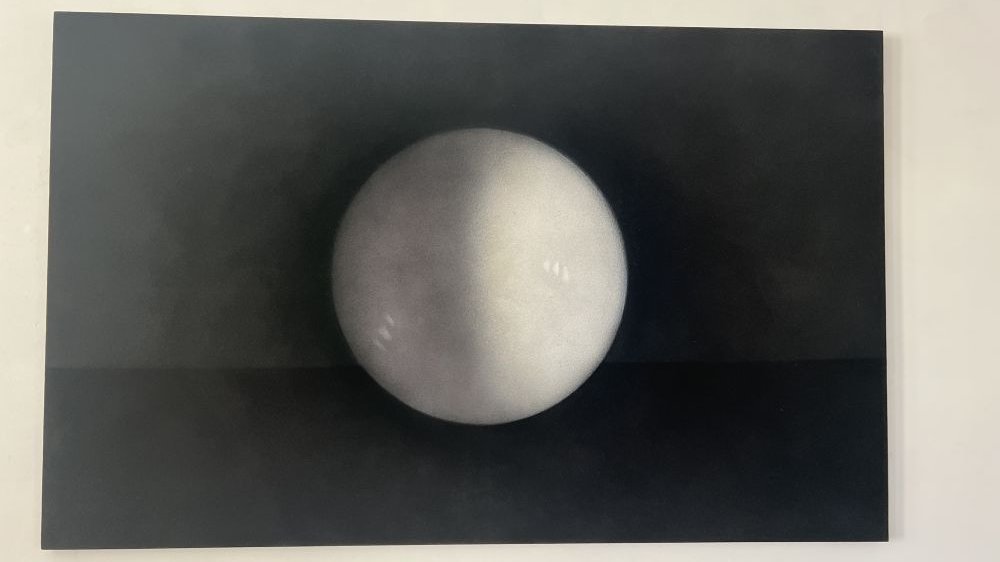 Na czarnym obrazie widnieje duża, biało-srebrzysta kula przypominająca księżyc w pełni.