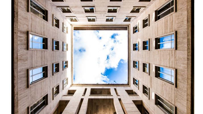 Fotografujący patrzy w górę, stoi idealnie w tym miejscu, w którym widać przeszklony sufit budynku, pokazujący błękitne, pogodne, pełne chmur niebo. Pod sufitem widać cztery ściany.
