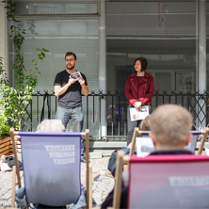 Scena na ul. Quadro, widzowie siedzą na leżakach. Na scenie dwie osoby.