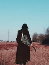 Foto. Kobieta z gitarą idzie przez pole.