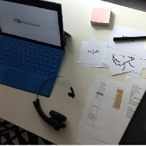 Laptop na stole, obok słuchawki, kartki, tablet, pisaki.