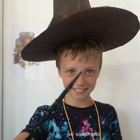 Uśmiechnięty chłopiec w kapeluszu czarodzieja z różdżką w dłoni.