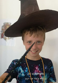 Uśmiechnięty chłopiec w kapeluszu czarodzieja z różdżką w dłoni.