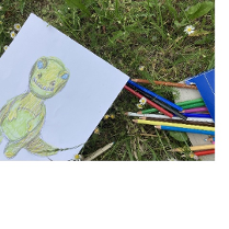 Na trawie kredki i rysunek dinozaura.