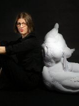 Krystyna Lipka-Czajkowska siedzi na podłodze, ręce położyła na kolanach, oparta o uszytą rzeźbę kobiety ułożonej w podobnej pozycji.