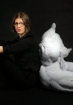 Krystyna Lipka-Czajkowska siedzi na podłodze, ręce położyła na kolanach, oparta o uszytą rzeźbę kobiety ułożonej w podobnej pozycji.