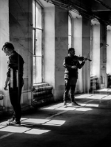 Czarno-biała fotografia złożona z kilku nałożonych na siebie kadrów. Kadry te przedstawiają dwóch mężczyzn z instrumentami. Muzycy są ujęci w różnych pozach, jeden z mężczyzn gra na skrzypcach.