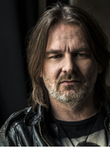 Fotografia przedstawia portret artysty patrzącego prosto w obiektyw.