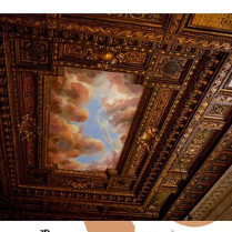 Widok zdobionego, rzeźbionego, drewnianego sufitu z malunkiem nieba i chmurami.