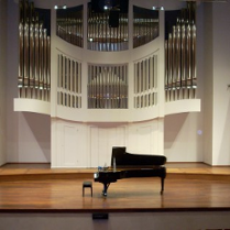 Na zdjęciu scena z fortepianem na środku. W tle piszczałki organów.