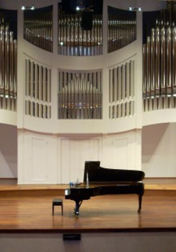Na zdjęciu scena z fortepianem na środku. W tle piszczałki organów.