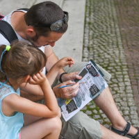 Ojciec z córką siedzą na schodach pochyleni nad broszurką.
