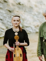 Fotografia ukazuje troje muzyków, dwie kobiety oraz mężczyznę, w tle znajduje się skaliste wzgórze. Cała trójka stoi przed aparatem trzymając instrumenty muzyczne, viola da gamba, vielle oraz lirę korbową. Łagodnie się uśmiechają.