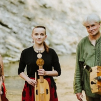 Fotografia ukazuje troje muzyków, dwie kobiety oraz mężczyznę, w tle znajduje się skaliste wzgórze. Cała trójka stoi przed aparatem trzymając instrumenty muzyczne, viola da gamba, vielle oraz lirę korbową. Łagodnie się uśmiechają.
