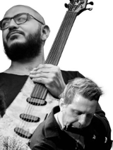 Grafika to kolaż czarno-białych portretów trzech muzyków. Jeden z nich trzyma gitarę, drugi gra na flecie poprzecznym, trzeci - na tabli.