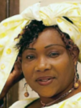 Na zdjęciu artyści: jedna kobieta i dwóch mężczyzn. Kobieta ma na sobie piękną, długą suknię w odcieniach jasnego żółtego i zieleni, a na głowie ozdobny turban. W dłoniach trzyma instrument muzyczny. Obok niej siedzą pozostali artyści, ubrani w ludowe kostiumy.