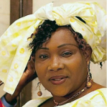 Na zdjęciu artyści: jedna kobieta i dwóch mężczyzn. Kobieta ma na sobie piękną, długą suknię w odcieniach jasnego żółtego i zieleni, a na głowie ozdobny turban. W dłoniach trzyma instrument muzyczny. Obok niej siedzą pozostali artyści, ubrani w ludowe kostiumy.