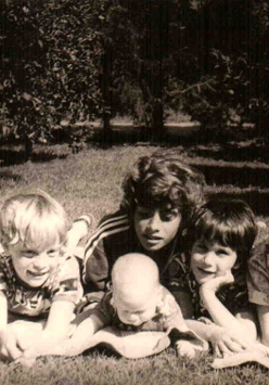 Fotografia przedstawiająca pięcioro dzieci leżące na kocu w sadzie.