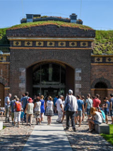 Budynek śluzy z czerwonej cegły. Na dachu trawa. Przed wejściem najprawdopodobniej wycieczka.