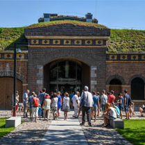 Budynek śluzy z czerwonej cegły. Na dachu trawa. Przed wejściem najprawdopodobniej wycieczka.