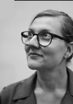 Na zdjęciu jest Marta Madejska, w portretowym ujęciu. Ma związane, gładko zaczesane włosy, okulary w wyrazistych oprawkach i marynarkę. Jej głowa skierowana jest w lewo, patrzy w górę z delikatnym uśmiechem.