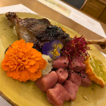 Zdjęcie, na talerzu noga gęsia, obok różowe kluseczki, kwiaty jadalne