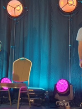 Dwóch mężczyzn na scenie. Jeden gra na dudach a drugi na bębnie. Na scenie stoją też lampy z pomarańczowym i różowym światłem. Z tyłu turkusowa kotara.