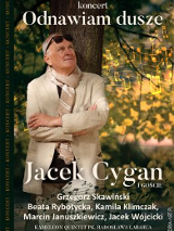 Na grafice Jacek Cygan w jasnej marynarce i szalem na szyi stoi pod drzewem..