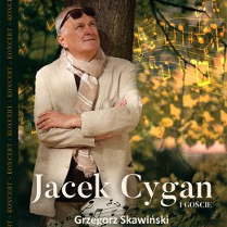 Na grafice Jacek Cygan w jasnej marynarce i szalem na szyi stoi pod drzewem..