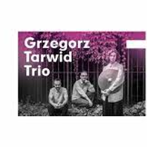 Grafika przedstawia czarno-białe zdjęcie trzech mężczyzn. Jeden z mężczyzn trzyma talerz od perkusji. Na górze pada na nich fioletowe światło.