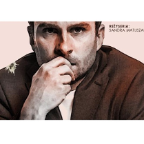 na bladoróżowym tle fragment postaci mężczyzny w brązowej marynarce. Mężczyzna trzyma dłoń przy ustach patrząc wprost w obiektyw, na ramieniu marynarka ma białą plamę.