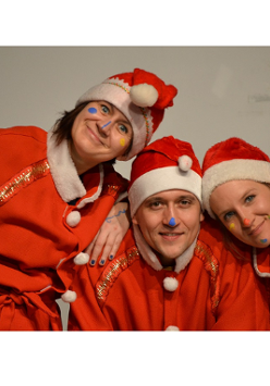 na zdjęciu trzy osoby ubrane w czerwone stroje Mikołaja, uśmiechnięte patrzą w obiektyw. Na nosach, brodzie i policzkach twarzach mają wymalowane kolorowe kropki.