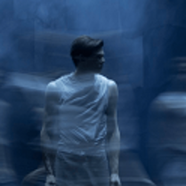 Zdjęcie stojącego mężczyzny, który patrzy w bok. Niebieskie, rozmyte tło.