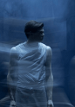 Zdjęcie stojącego mężczyzny, który patrzy w bok. Niebieskie, rozmyte tło.