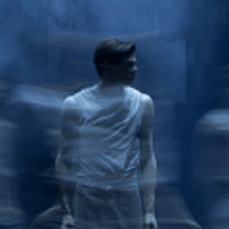 Zdjęcie stojącego mężczyzny, który patrzy w bok. Niebieskie, rozmyte tło.