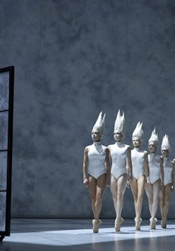 na zdjęciu po lewej stronie chłopiec patrzący przez duże okno, przed oknem rząd baletnic w białych strojach typu body i białych nakryciach głowy