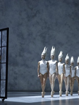 na zdjęciu po lewej stronie chłopiec patrzący przez duże okno, przed oknem rząd baletnic w białych strojach typu body i białych nakryciach głowy