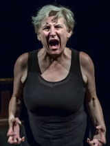 na zdjęciu kobieta w średnim wieku patrzy w obiekty i krzyczy głośno, ręce ma skierowane do przodu, place zagięte