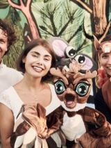 Zdjęcie trójki aktorów, którzy trzymają lalki - bohaterów spektaklu Grajmy w zielone. Aktorzy stoją na tle rysunkowego lasu.