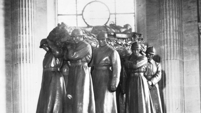Czarno-białe zdjęcie nagrobka. Na sarkofagu pomnik przedstawiający żołnierzy niosących ciało marszałka Focha leżące na katafalku.