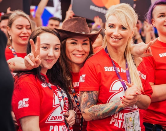 Grupa dziewczyn w czerwonych kuszulkach służby informacyjnej WOŚP uśmiecha się do obiektywu.