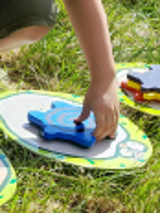 na trawie rozrzucone kolorowe dyski, na nich piankowe gwiazdki, które ktoś chwyta w dłoń