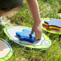 na trawie rozrzucone kolorowe dyski, na nich piankowe gwiazdki, które ktoś chwyta w dłoń