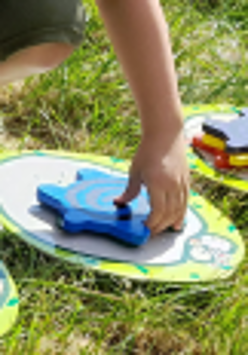 na trawie rozrzucone kolorowe dyski, na nich piankowe gwiazdki, które ktoś chwyta w dłoń