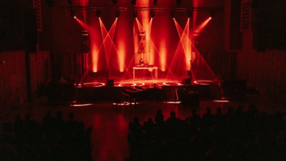 Artysta na scenie w czerwonym świetle, publiczność pogrążona w mroku.
