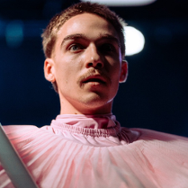 Zdjęcię mężczyzny w różowym stroju, który trzyma szary rurę.