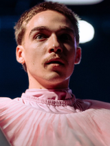 Zdjęcię mężczyzny w różowym stroju, który trzyma szary rurę.