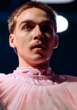 Zdjęcię mężczyzny w różowym stroju, który trzyma szary rurę.